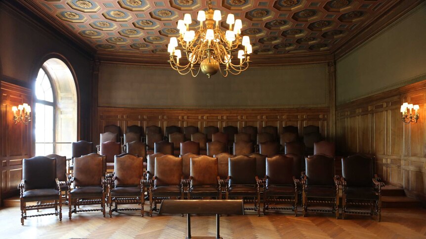 Rows of leather chairs face towards the camera in a wood panelled room.