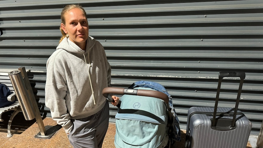 A woman in a tracksuit stands next to a pram and suitcase. 