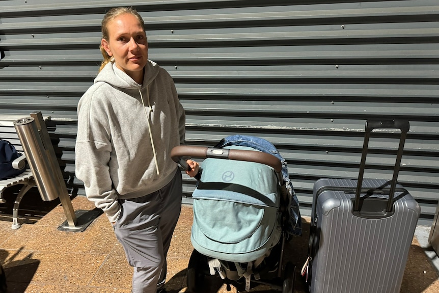A woman in a tracksuit stands next to a pram and suitcase. 