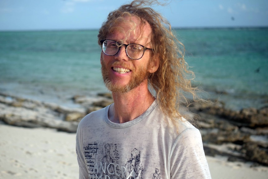 Portrait of David Adams on the beach with brilliant sea behind him