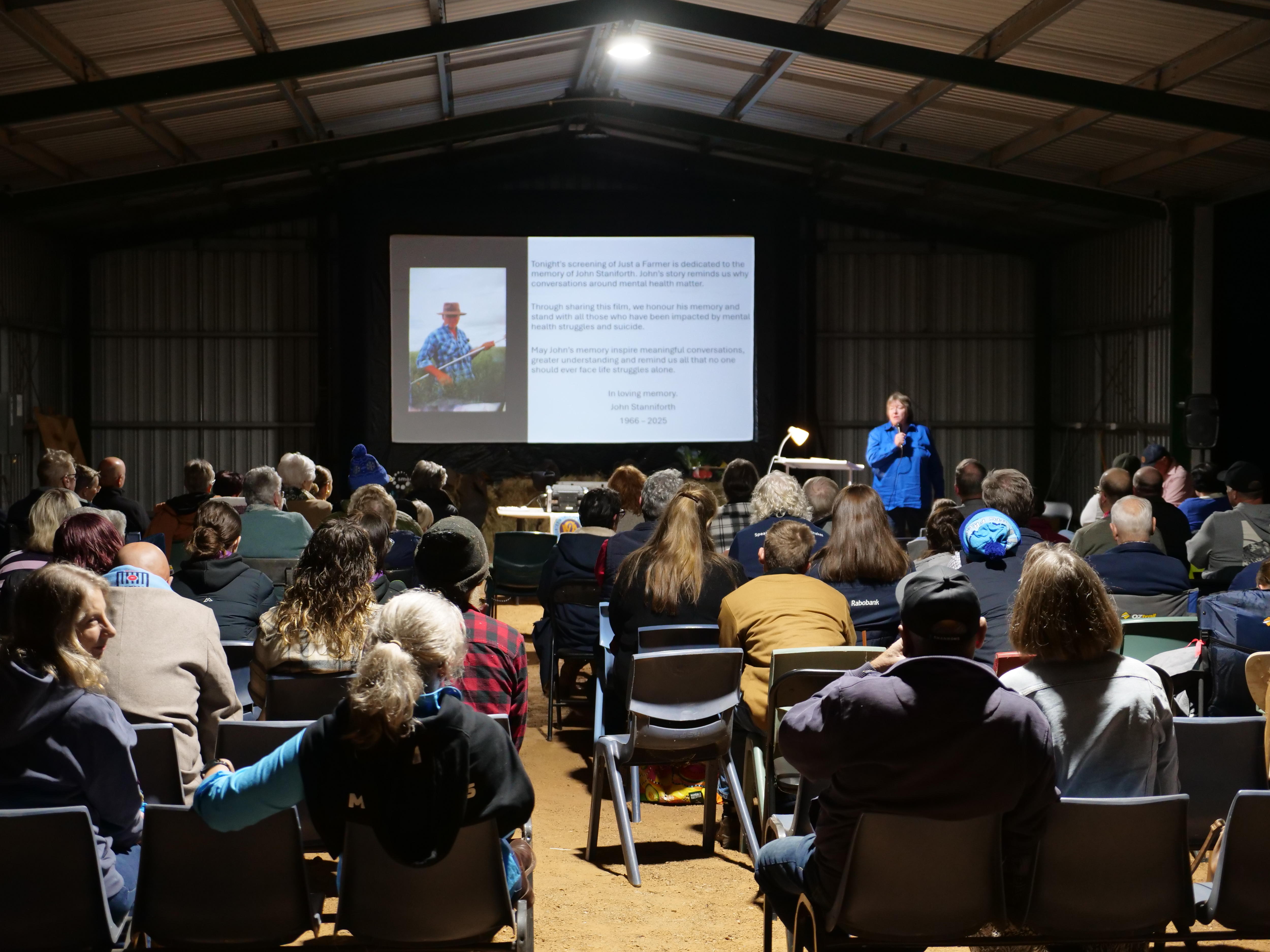 A view of people watching a movie in a large tin shed.