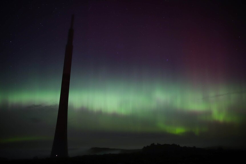 The southern lights shimmer over a thick level of cloud.