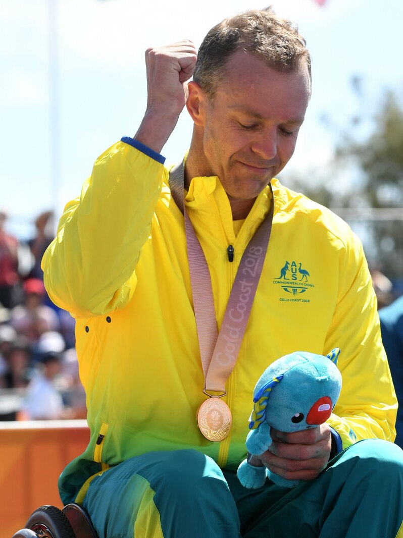 Bronze medallist Bill Chaffey looks down, pumping his left fist in the air and holding a blue toy in his other hand.
