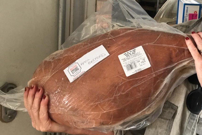 Jo Wheaton holding up one of their plastic wrapped Christmas hams