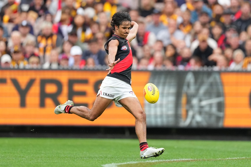 Alwyn Davey de Essendon mira hacia abajo mientras deja caer el balón en su bota para una patada de gol desde afuera de los 50.