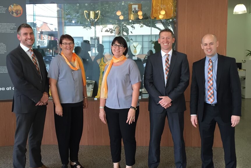 Cinq administrateurs sportifs posent pour une photo en gris et orange