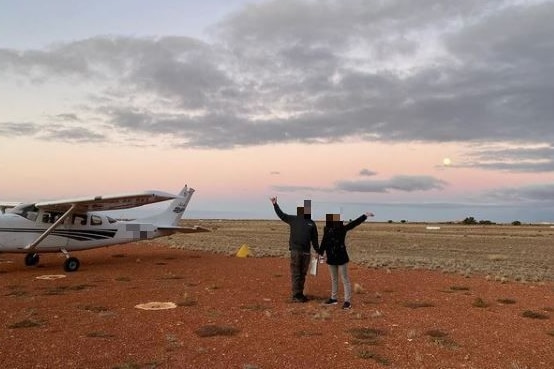 Two people next to a small plane on red dirt