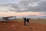 Two people next to a small plane on red dirt