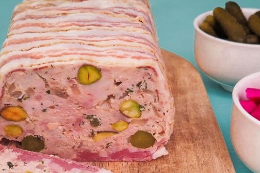 A slice of rabbit terrine cut from a rectangular loaf on a chopping board.
