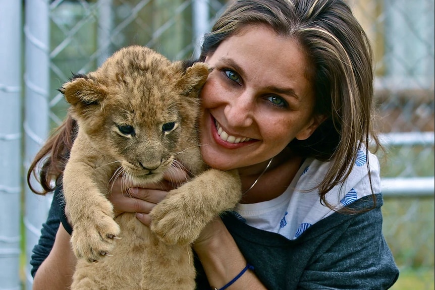 Smiling woman holding lion cub. 