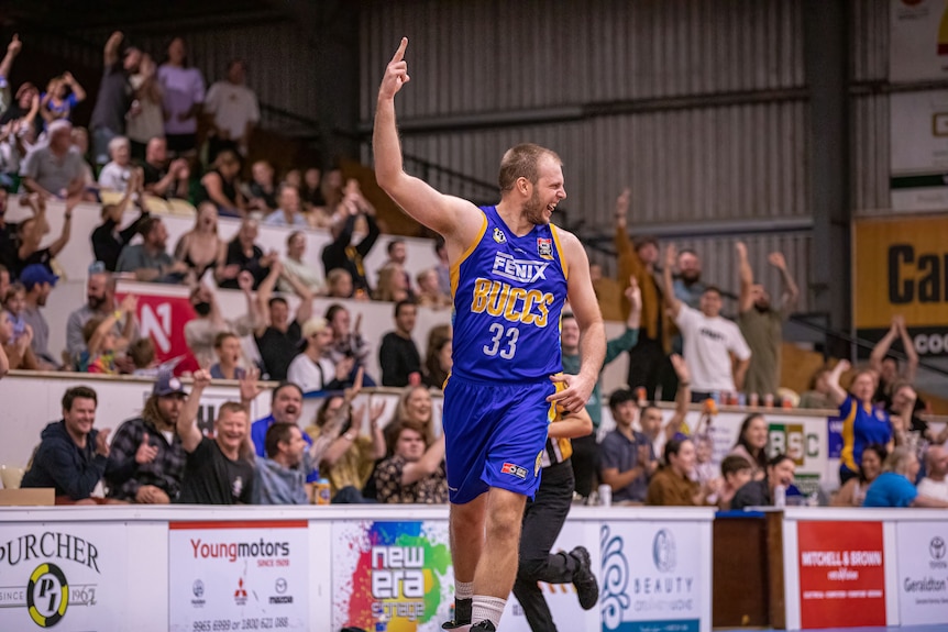Man in blue basketball uniform smiles and raises his hand in the air in victory celebration 