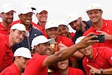 The US golf team huddles together to take a selfie with the Presidents Cup trophy