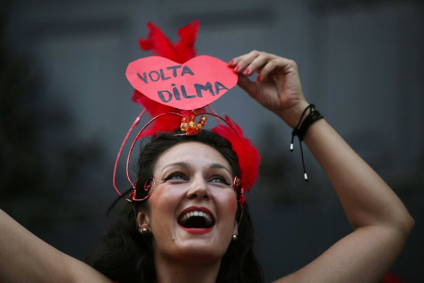 A woman wears a Carnival hat with a sign reading 'Return Dilma', referring to a former president of Brazil.
