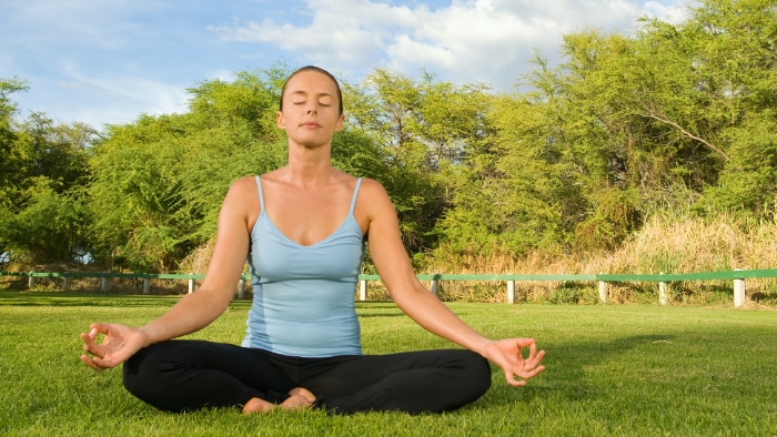 A woman sitting outside on the grass in the lotus yoga pose.