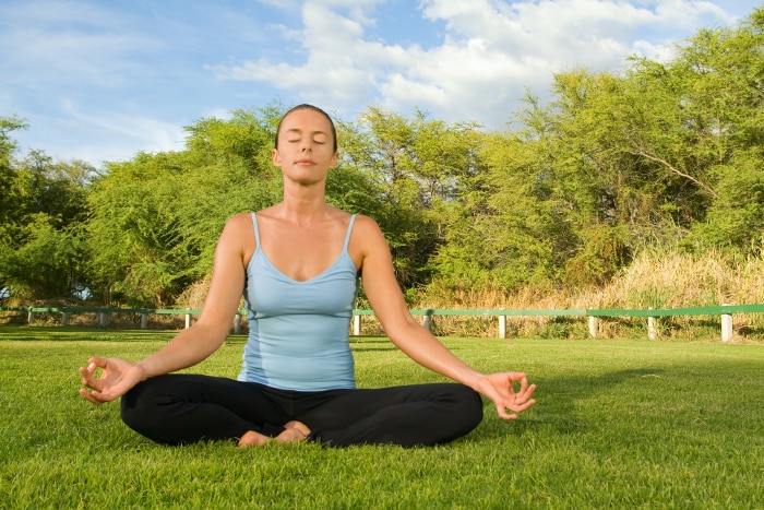 A woman sitting outside on the grass in the lotus yoga pose.