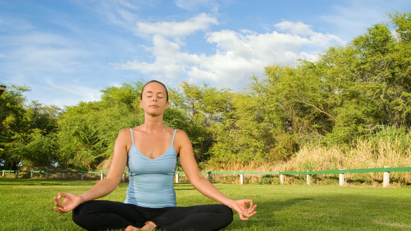 A woman in a blue outfit sitting in the lotus meditation pose.