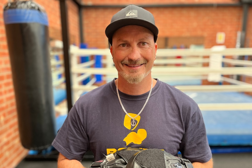 A man wearing boxing gloves and a baseball cap smiles