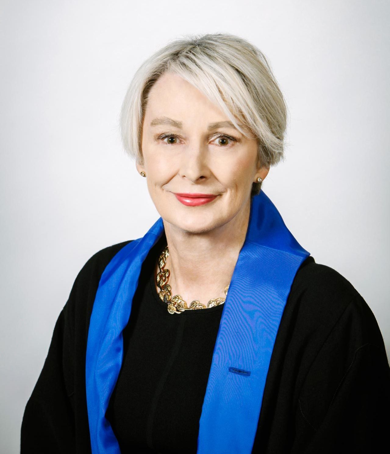 A woman with short grey hair wearing a black top and a blue scarf 