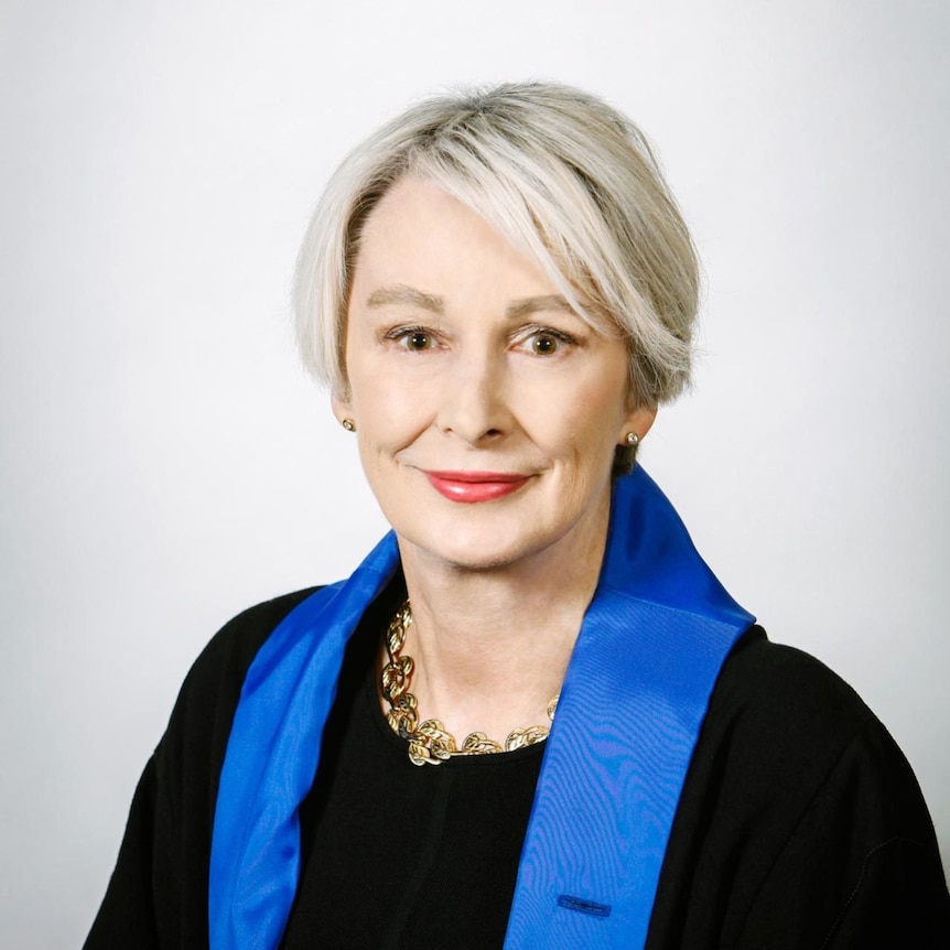 A woman with short grey hair wearing a black top and a blue scarf 