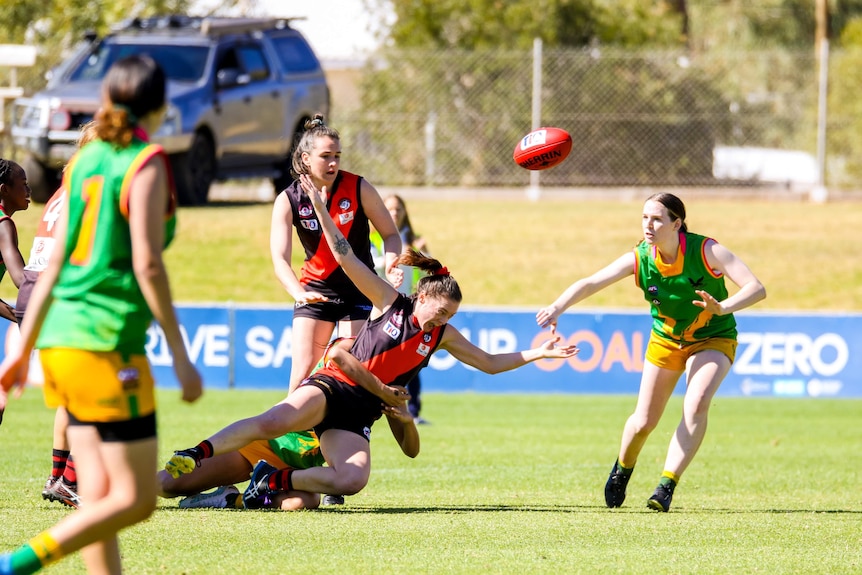 A woman is tackled to the ground in a game of footy