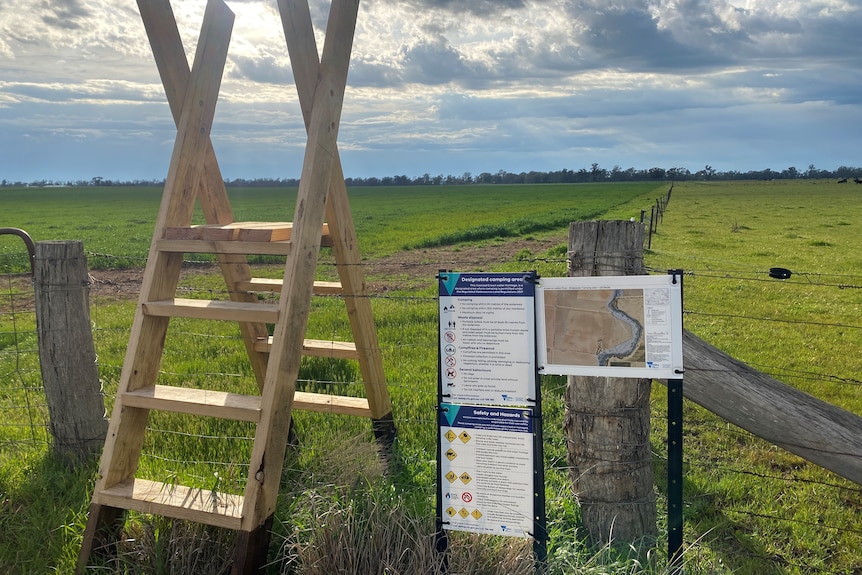 A wooden step ladder sits over a fence, information signs sit alongside. 