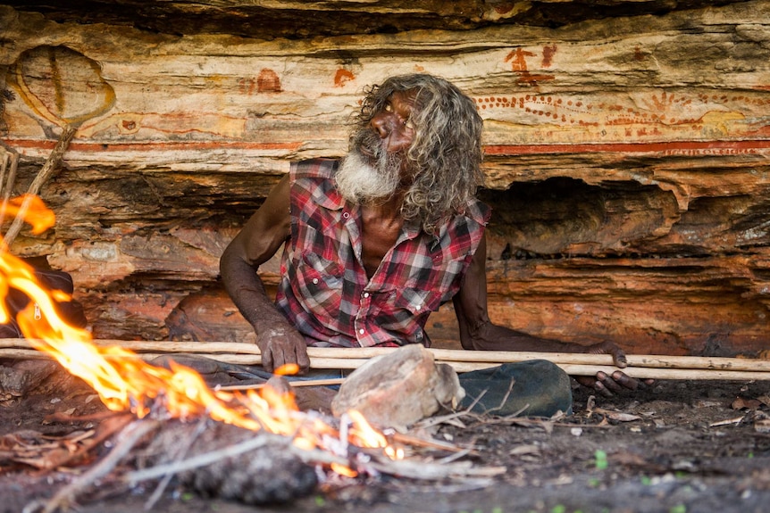 A film still showing Dalaithngu sitting behind a fire.