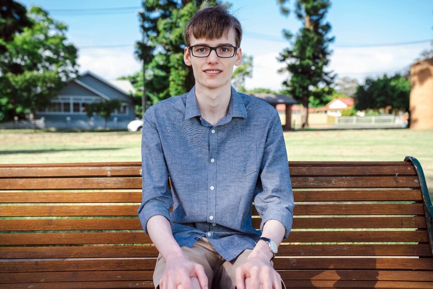 Myles, a young man, sits on a park bench smiling at the camera