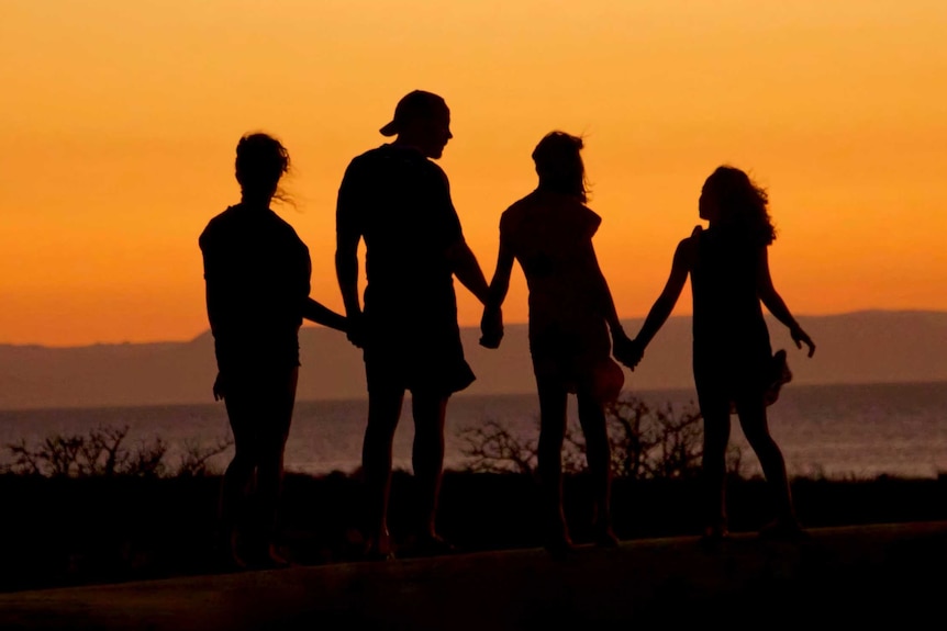 Famille tenant la main se découpant sur le coucher du soleil
