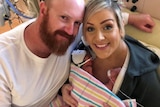 A bald man with a beard and a blonde woman holding two premature babies in a blanket