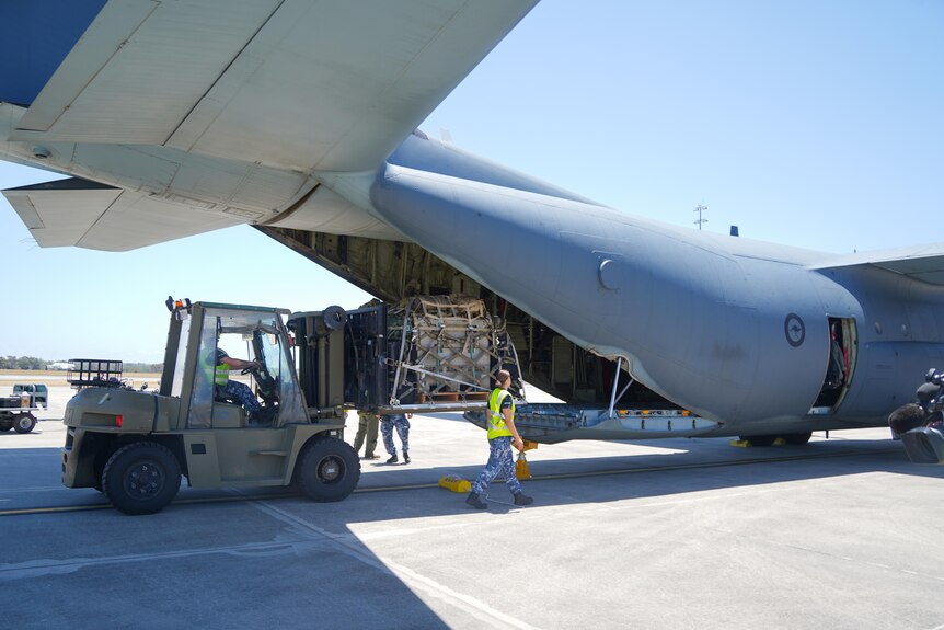 The rear end of a military plane being loaded with supplies. 