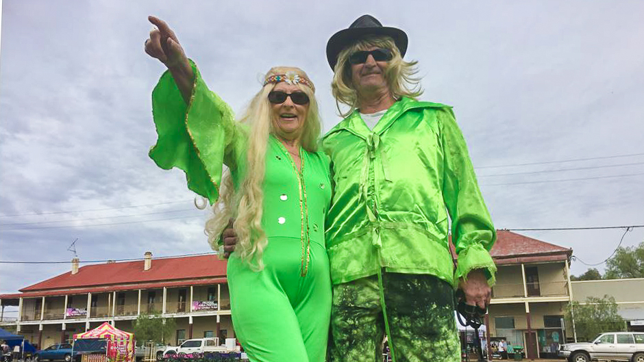 A man and womn in bright green costumes including the woman in a jumpsuit and long blonde wig in front of a country pub