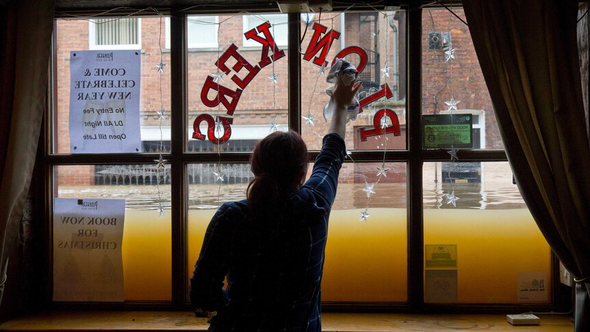 A woman cleans the inside of a window as floodwaters, outside, sit halfway up the window.