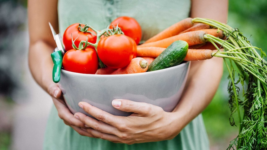 Close-up of a woman holding a bowl of freshly harvested vegetables