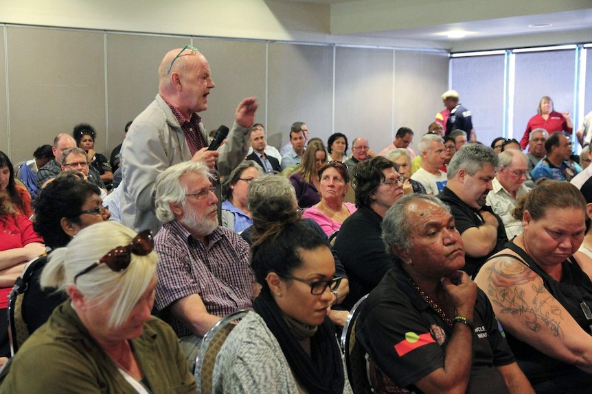 A man holding a microphone addresses a room of people