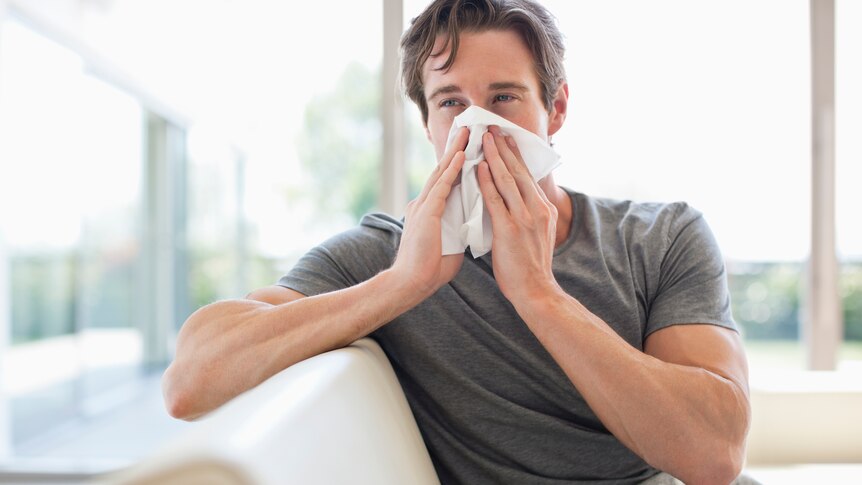 man on couch blowing his nose