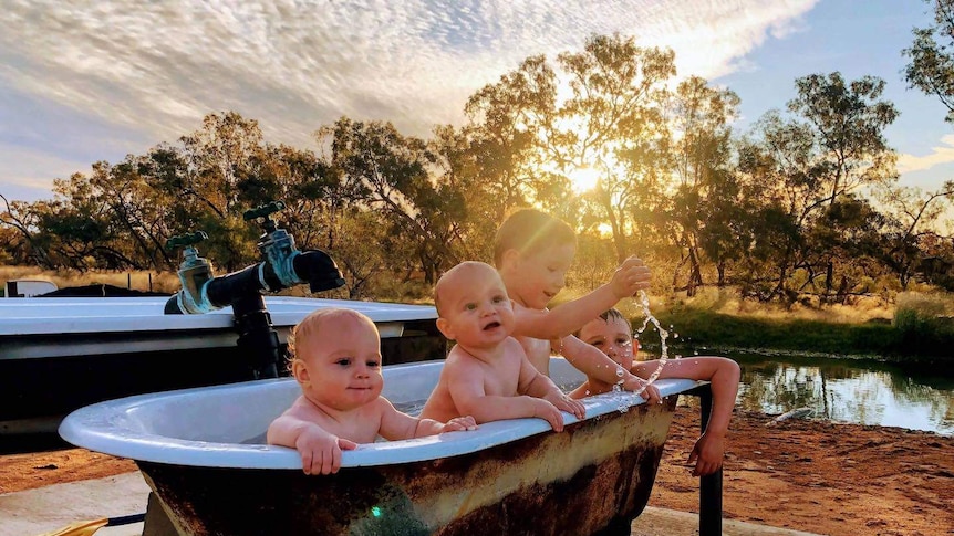 Four young children sit in an outdoor bath on the edge of a river.