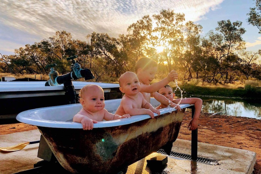 Four young children sit in an outdoor bath on the edge of a river.