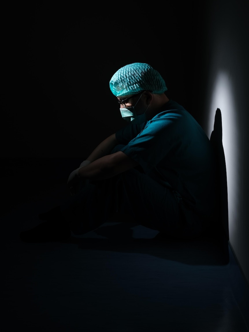 Dark backdrop, a doctor sits slumped in surgical attire