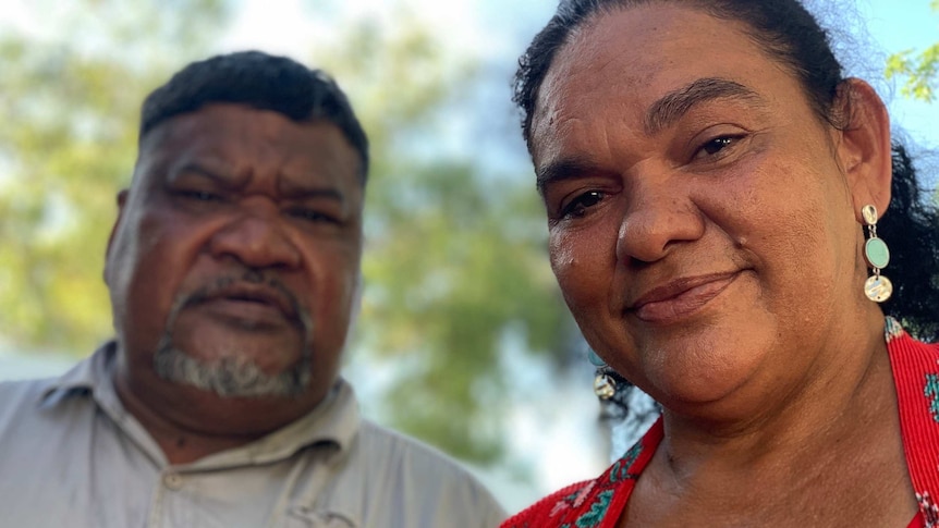 Close-up image of an Indigenous woman wearing a red dress, with an Indigenous man standing in the background.