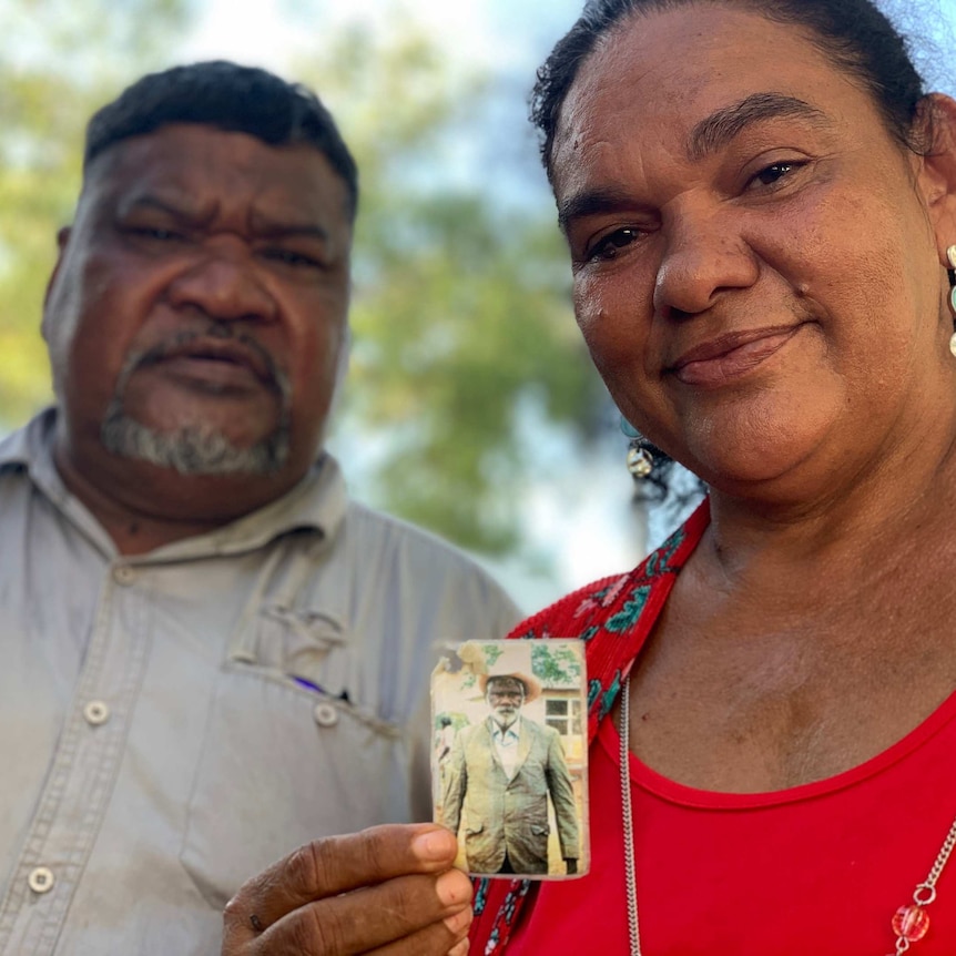 Close-up image of an Indigenous woman wearing a red dress, with an Indigenous man standing in the background.