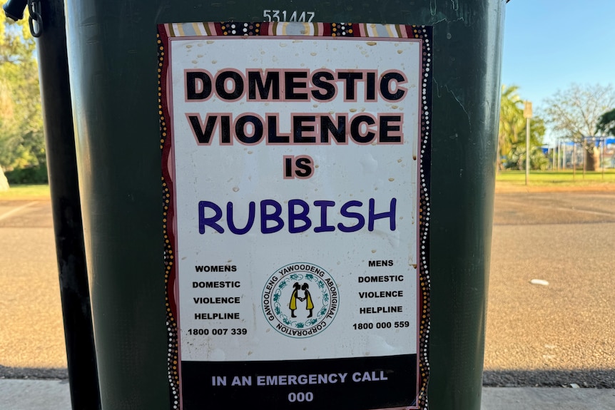 a poster saying domestic violence is rubbish is taped to a bin