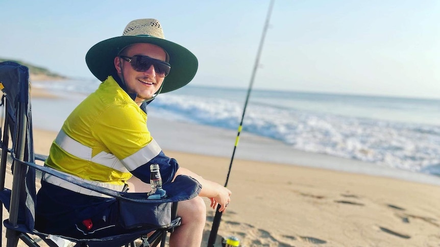 Man sits in a camping chair with a fishing rod on the beach. 