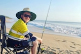 Man sits in a camping chair with a fishing rod on the beach. 