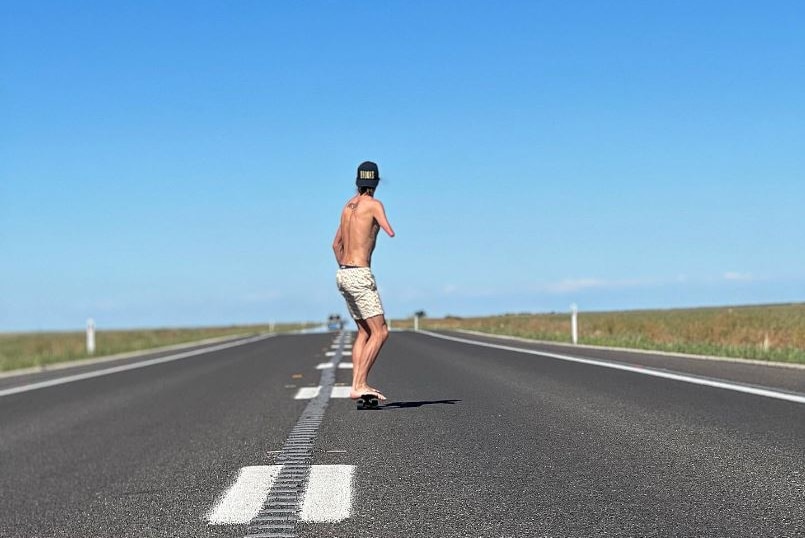 Michael Roeger is riding a skateboard down a road