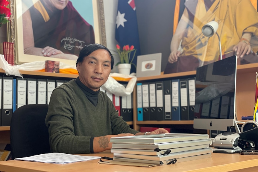 Migmar Tsering sits at a desk in front of a picture of the Dalai Lama.
