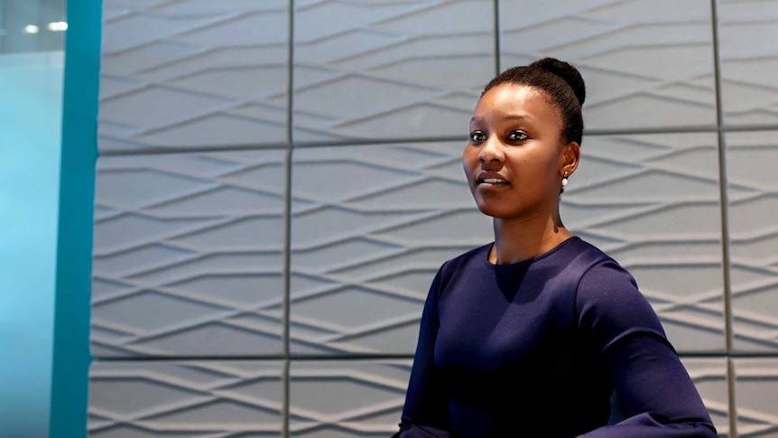 Nasilele wearing blue top, hair in a bun, sitting in a corporate office.