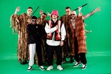 Members of a musical group wearing colourful clothing stand in front of a green screen to film a video.