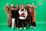 Members of a musical group wearing colourful clothing stand in front of a green screen to film a video.