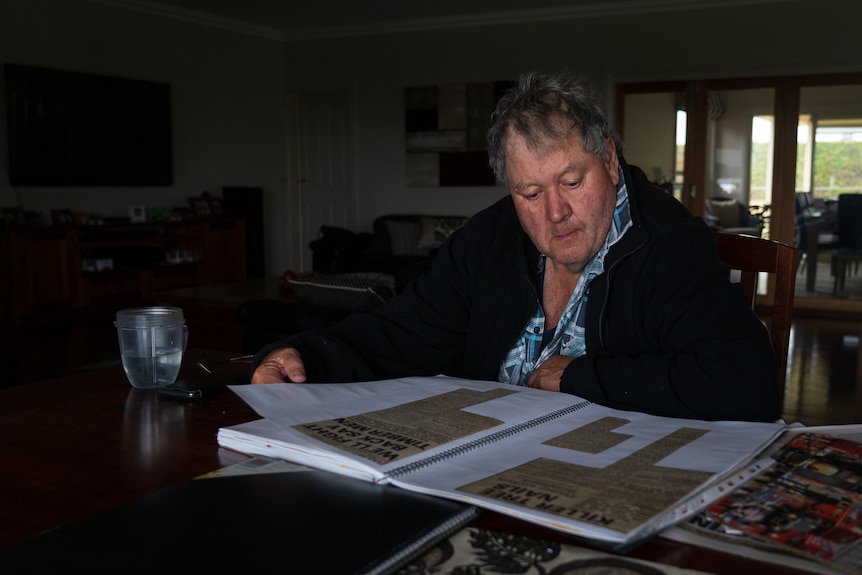 A man looks at a scrapbook of newspaper articles.