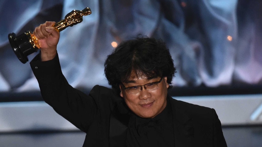 Bong Joon Ho holds his Oscar for best international feature film in the air while on stage at the Academy Awards.